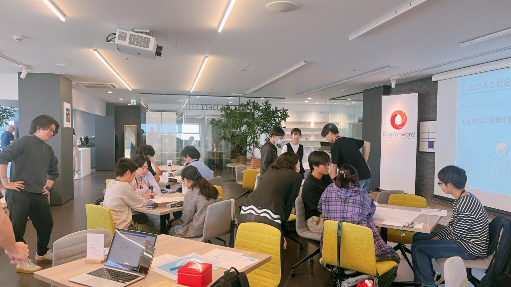写真。教室となる企業のオフィスで10〜20名の受講生やメンターがワイワイ話している。
