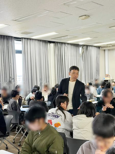 写真。東京都立産業技術高等専門学校の教室で、生徒の中を歩く代表濱。