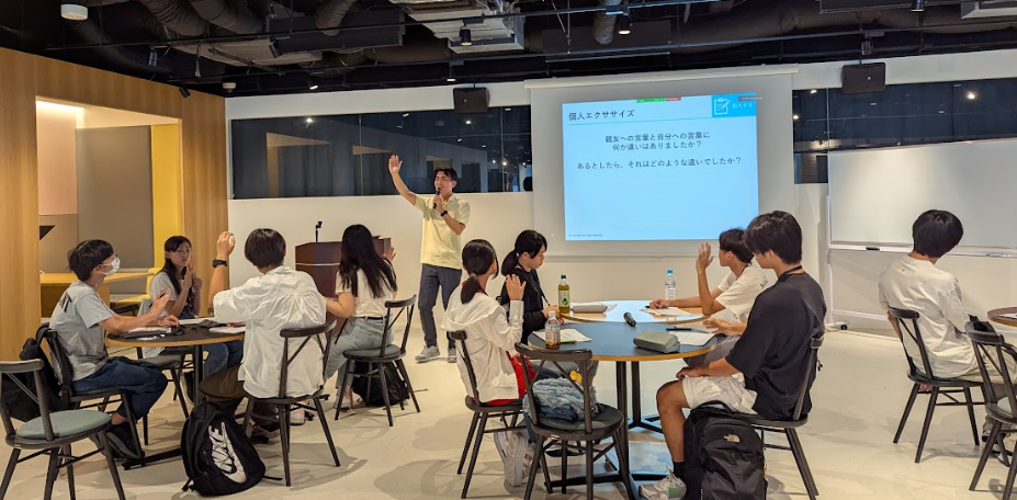 写真。講師が片手を挙げ、受講生に向かって挙手を促している。