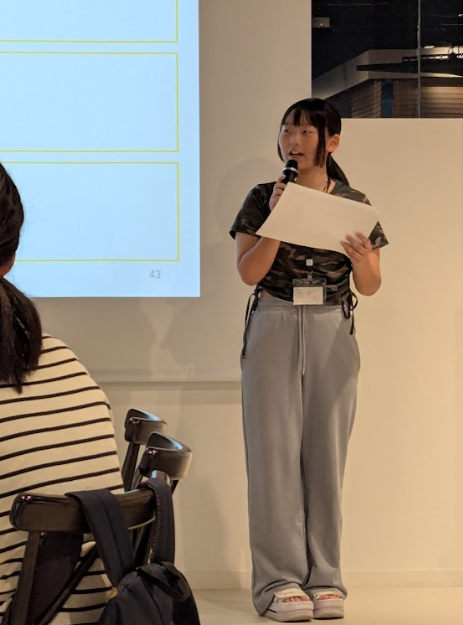 写真。プロジェクタ前で発表する受講生。